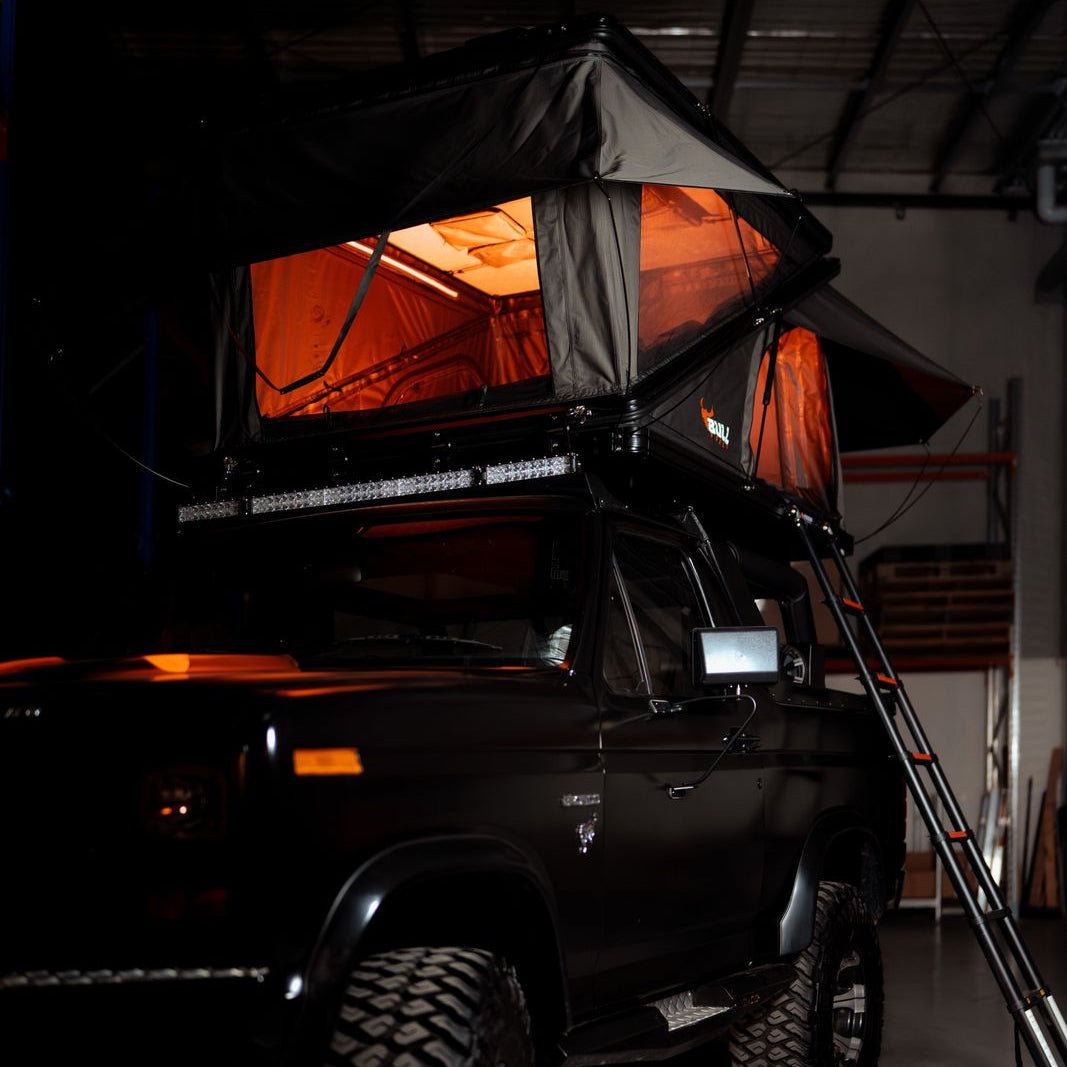Summit XLZ rooftop tent lit with orange light on a black 4x4 with roof bars and ladder